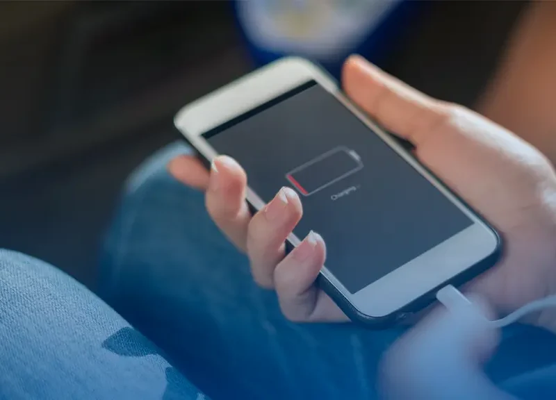 Person holding a smartphone connected to a charger; low battery icon displayed on screen.